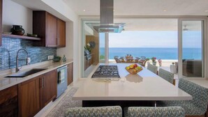 Une cuisine moderne dotée d’un grand îlot central, d’un coin repas offrant une vue sur l’océan et d’un balcon avec un espace salon extérieur.