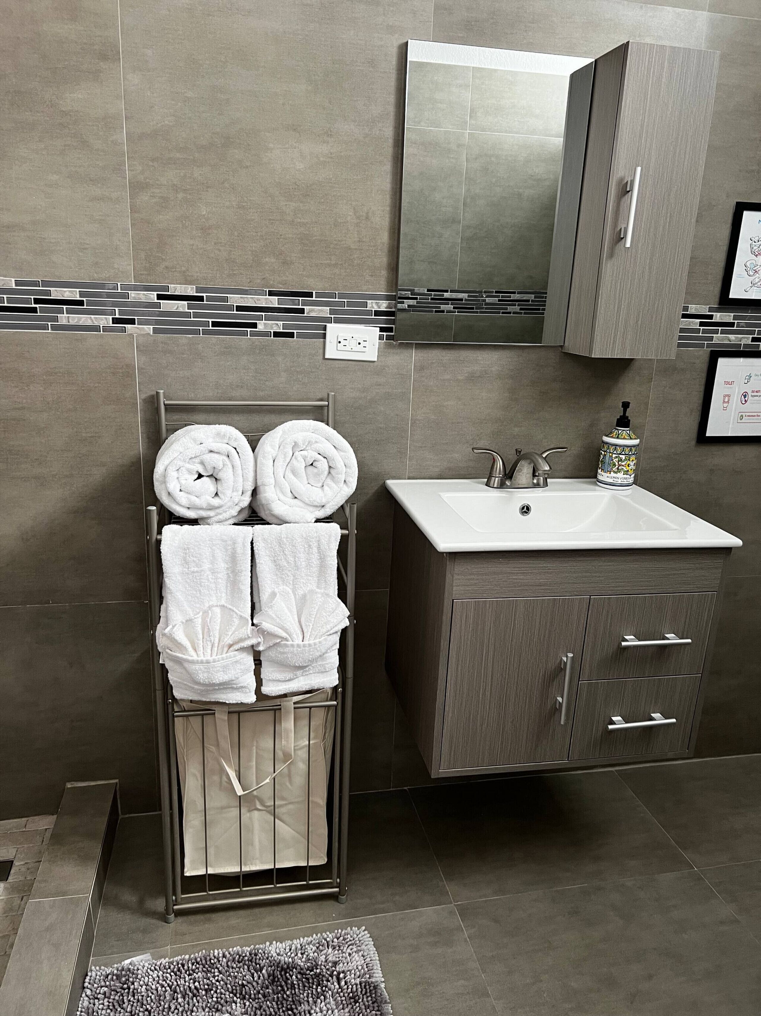 Une salle de bain moderne avec un grand lavabo, un porte-serviettes où sont pliés soigneusement les serviettes, un miroir au-dessus du lavabo et un pare-éclaboussures carrelé.