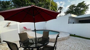 An outdoor pool area with a round table and four chairs, a red umbrella, and a red lounge chair. - Charming apartment 5' walk to the beach (Carolina)