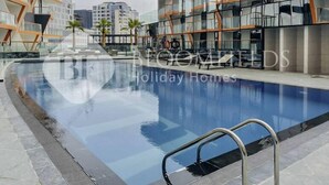 A modern building with a glass facade and a swimming pool in front. - 122 Bloomfields Cozy1BR Binghatti Avenue (Dubai)