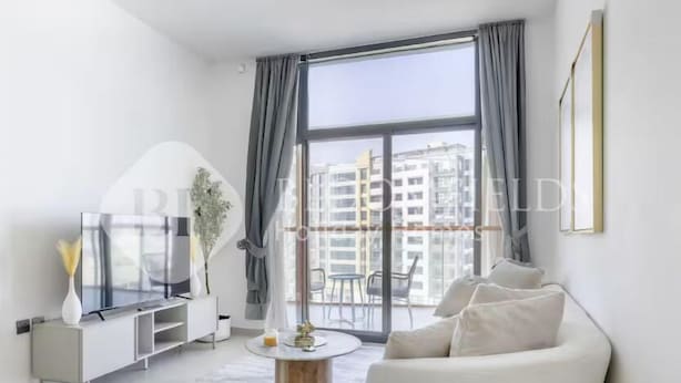 A modern living room with a large window, a white sofa, a TV on a white cabinet, and a round coffee table. - 122 Bloomfields Cozy1BR Binghatti Avenue (Dubai)
