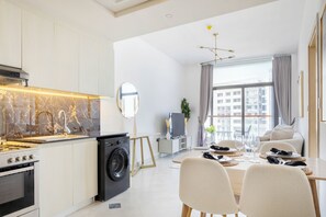 A modern kitchen with a stove, washing machine, and a dining area with a table and chairs. - Bloomfields 1BR in Binghatti Avenue-Jaddaf (Dubai)