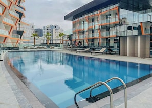 A swimming pool with lounge chairs and a modern building with orange accents.