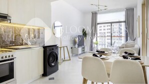 A modern kitchen with a built-in stove, a washing machine, and a dining area with a table set for two. - 122 Bloomfields Cozy1BR Binghatti Avenue (Dubai)