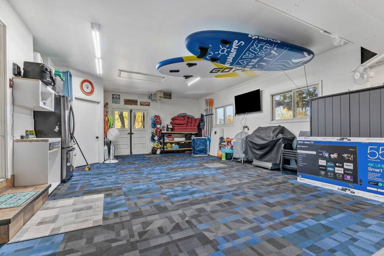 Une pièce avec une moquette à motifs, un ventilateur de plafond, un téléviseur et une étagère fixée au mur.