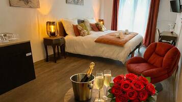 Une chambre d’hôtel avec un lit, un bureau, une chaise, une table sur laquelle se trouve une bouteille de champagne, des verres et un bouquet de roses rouges.