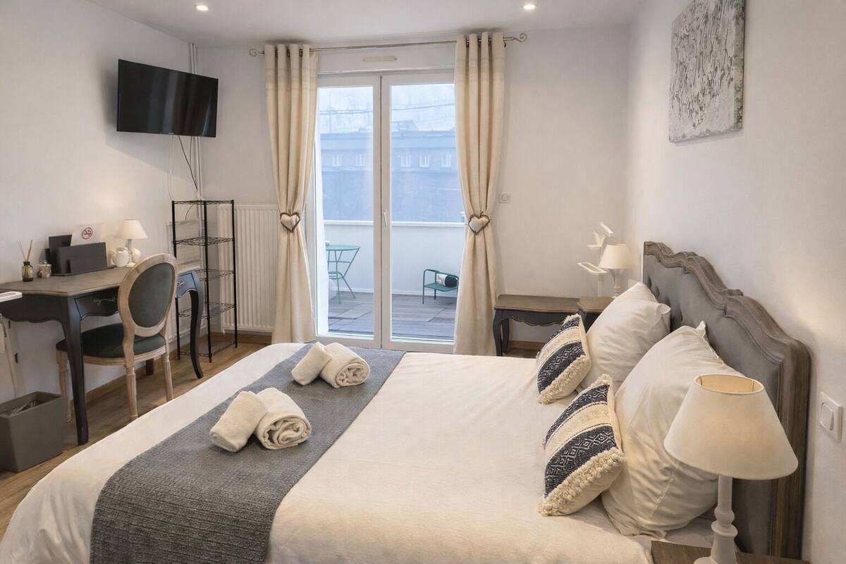 Habitación de hotel con cama, mesitas de noche, escritorio, silla, televisión y vistas al exterior.