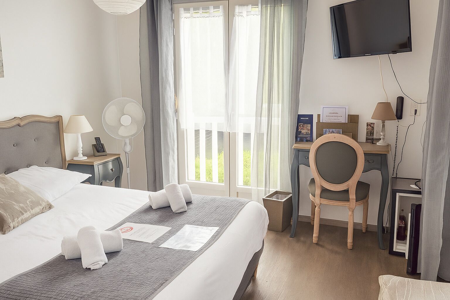 Une chambre d’hôtel équipée d’un lit, d’un bureau, d’une chaise, d’une télévision et d’une fenêtre avec des rideaux.