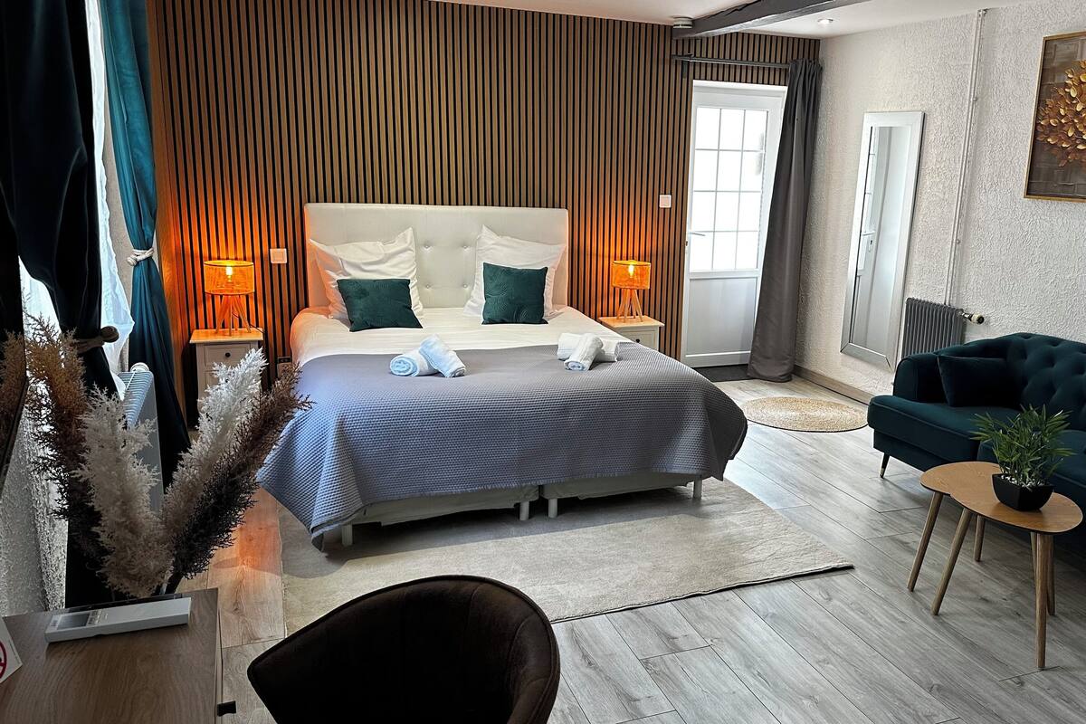 Un dormitorio moderno con una cama grande, un sofá verde oscuro y una pequeña mesa con una planta.