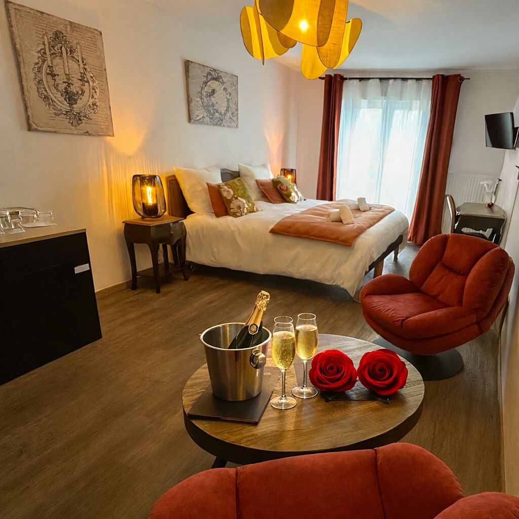 Ein Hotelzimmer mit Bett, Schreibtisch, Stuhl, Tisch mit Champagnerflasche, Gläsern und Rosen.