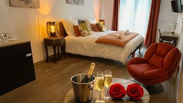 Ein Hotelzimmer mit Bett, Schreibtisch, Stuhl, Tisch mit Champagnerflasche, Gläsern und Rosen.