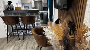 A modern kitchen with a stone accent wall, a wooden dining table with chairs, and a decorative plant arrangement. - Logis Hôtel Blue Garden (Grandvillers)