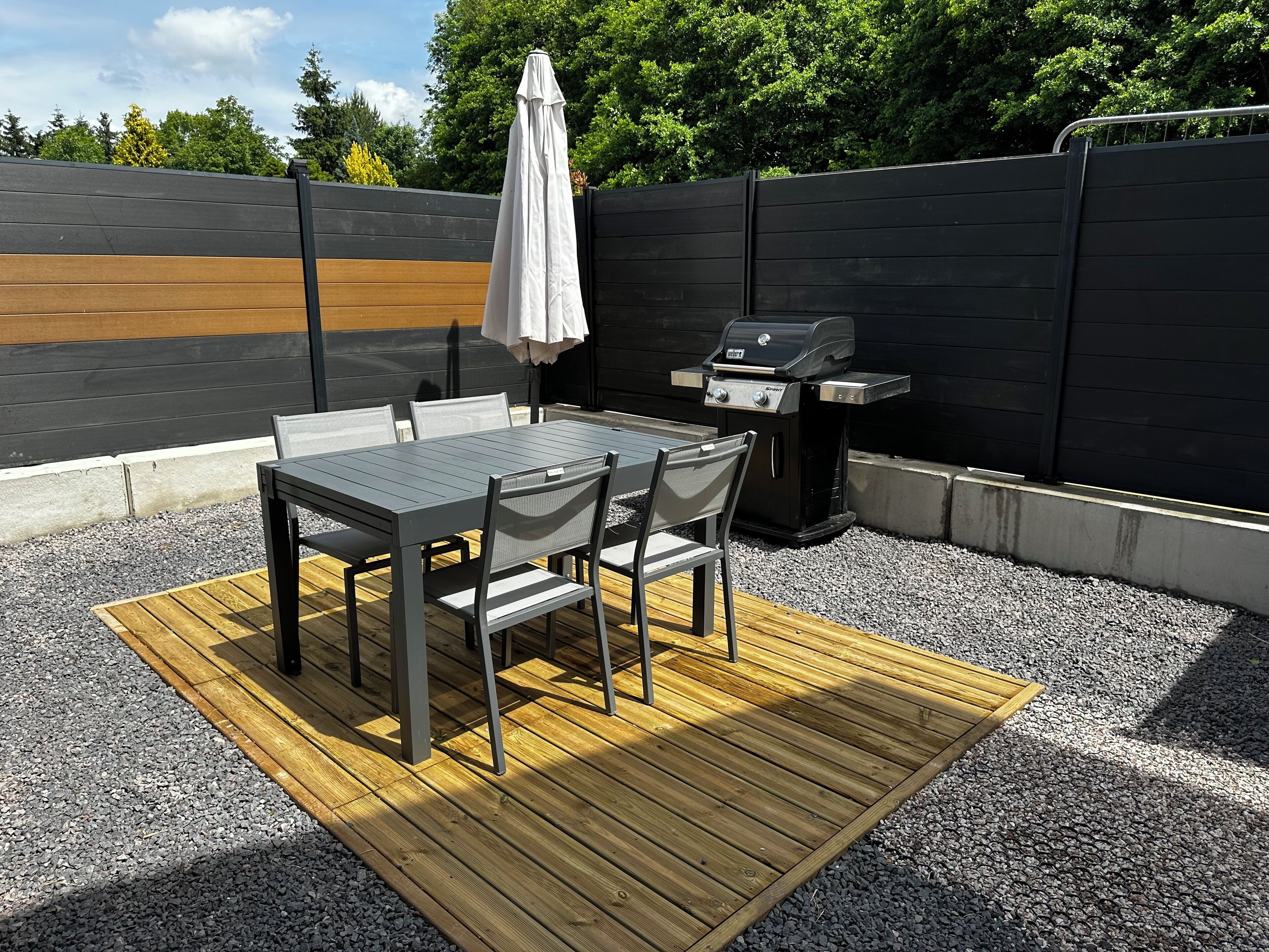 A patio with a table and chairs, a grill, and a wooden deck.