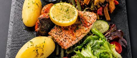 A meal consisting of grilled salmon, roasted vegetables, potatoes, and a side salad on a slate plate.