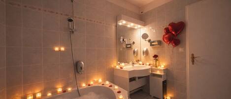 A bathroom with a bathtub surrounded by candles, a shower, and a vanity with a mirror.