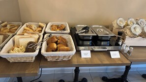 Een buffet met diverse etenswaren, waaronder brood, gebak en toevoegingen.