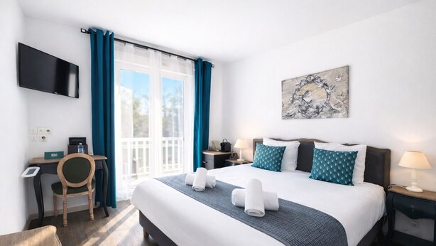 A hotel room with a bed, a desk, a chair, a TV, and a painting on the wall. - Logis Hôtel Blue Garden (Grandvillers)