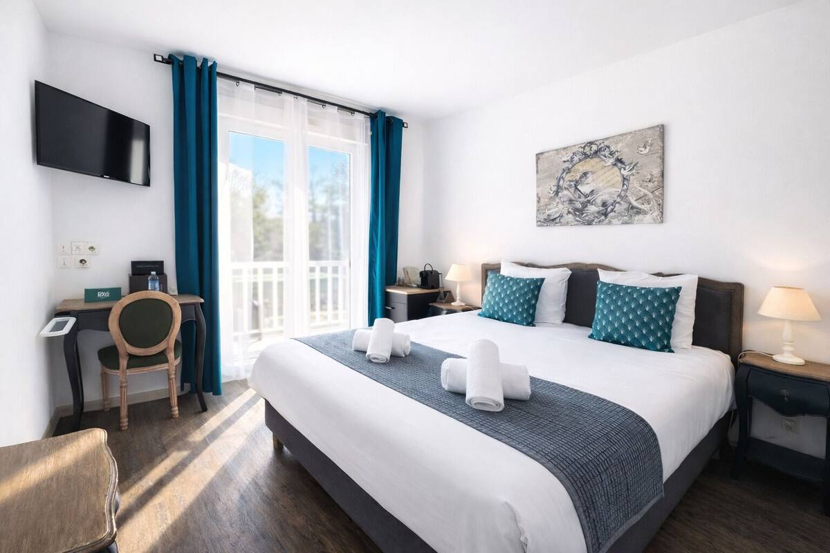 Una habitación de hotel con una cama, un escritorio, una silla, un televisor y un cuadro en la pared.