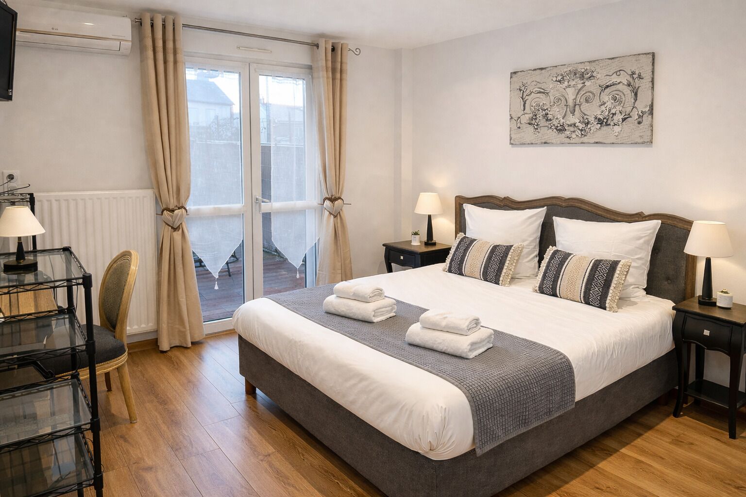 Een hotelkamer met een groot bed, twee nachtkastjes met lampen, een bureau met stoel, en uitzicht door een glazen deur.