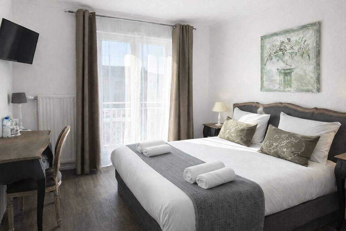 Una habitación de hotel con una cama, un escritorio, una silla, un televisor y un cuadro en la pared.