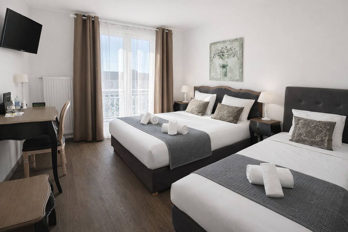 Habitación de hotel con dos camas, un escritorio, una silla, un televisor y una ventana con cortinas.