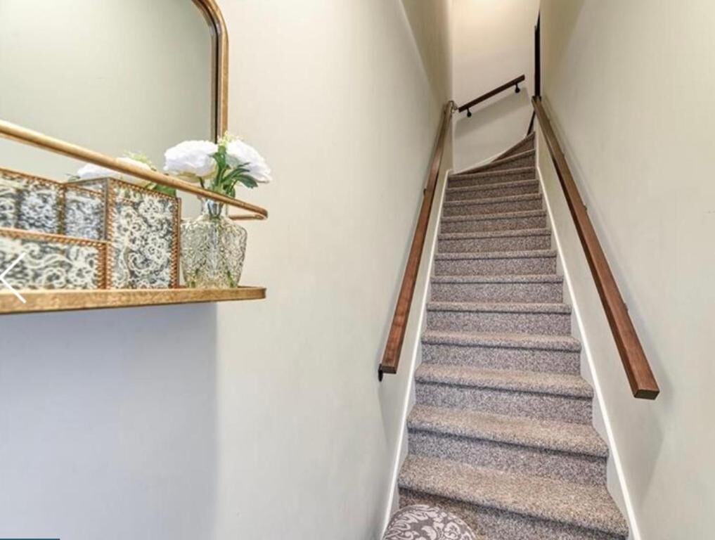 Un escalier recouvert de moquette, doté d’une rampe en bois et d’une étagère fixée au mur, ornée d’objets décoratifs.