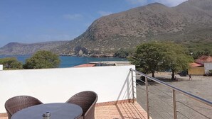 A terrace with wicker furniture, a table, and a view of the sea and mountains. - Hotel Strela Tarrafal (Tarrafal)
