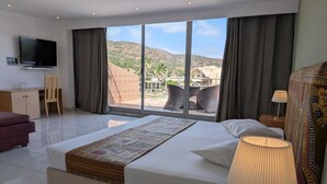A hotel room with a large bed, a desk, a TV, and a view of the mountains. - Hotel Strela Tarrafal (Tarrafal)