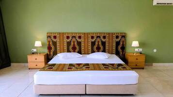 A double bed with a patterned headboard, two bedside tables with lamps, and a green wall with an air conditioning unit.