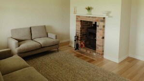 A living room with a beige sofa, a fireplace, and a rug. - Cosy 2 bedroom cottage with rural farmland views (Ross Creek)