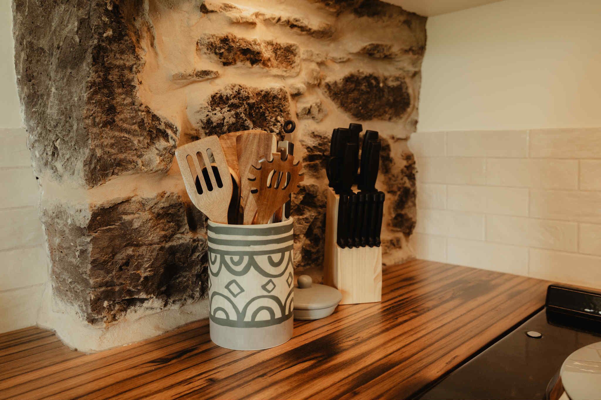 Un plan de travail de cuisine avec un mur en pierre, un porte-ustensiles à motifs et un bloc à couteaux.