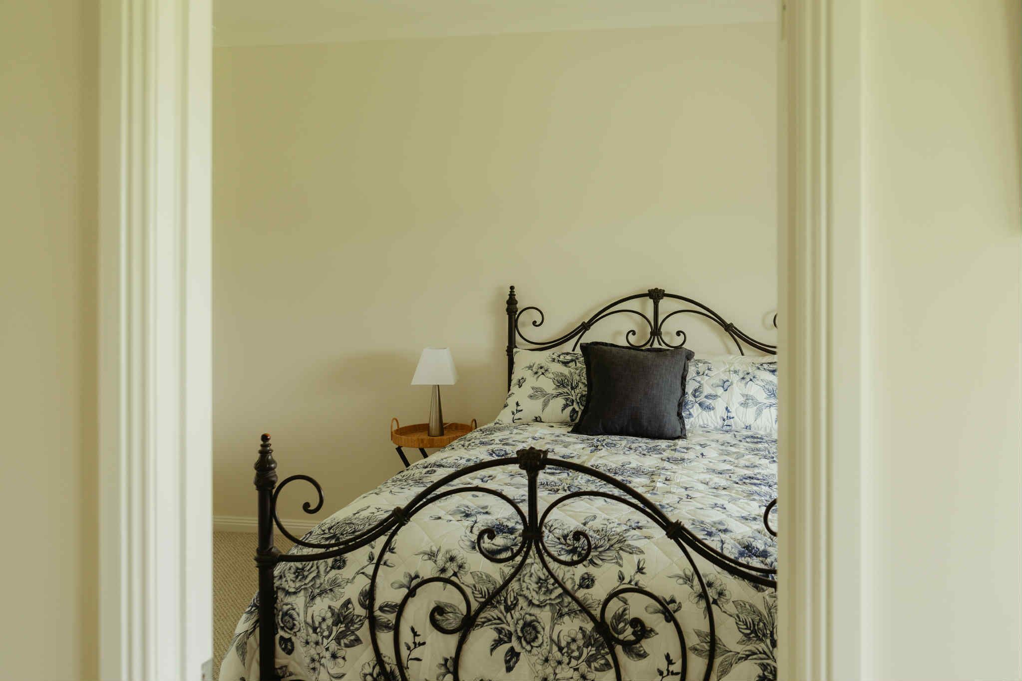 Ein Bett mit blumigem Überwurf, einem schwarzen Metall-Kopfstück und einem kleinen Nachttisch mit Lampe.