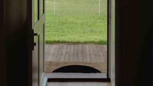 An open door leading to a grassy outdoor area with a wooden deck and a doormat. - Cosy 2 bedroom cottage with rural farmland views (Ross Creek)