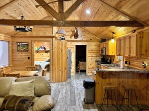 A cozy cabin interior with a dining area, kitchen, and a living room with a sofa and chairs.