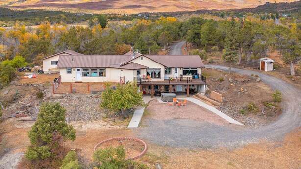 A two-story house with a patio and a deck, surrounded by a natural landscape with hills in the background.