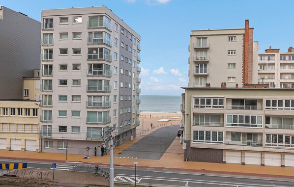 Un immeuble à plusieurs étages offrant une vue sur la plage, doté de balcons et d’une promenade piétonne menant à la plage.
