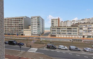 Une zone urbaine côtière comprenant des immeubles résidentiels à plusieurs étages, une promenade piétonne et une route bordée de voitures garées.