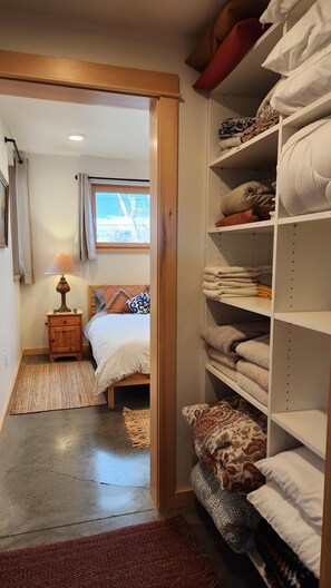 Ein Schlafzimmer mit Bett, Nachttisch, Lampe und einem Kleiderschrank mit Regalen voller gefalteter Handtücher.