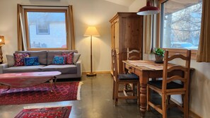Ein gemütliches Wohnzimmer mit Sofa, Couchtisch, Esstisch mit Stühlen, einer Lampe und einem Fenster mit Aussicht.