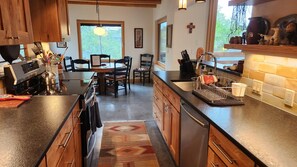 A modern kitchen with wooden cabinets, a stainless steel dishwasher, and a dining area with a table and chairs. - Close to everything Bozeman! (Bozeman)