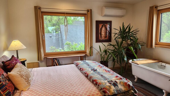 A bedroom with a bed, a window, a bedside lamp, a bookshelf, a potted plant, and a white bathtub. - Close to everything Bozeman! (Bozeman)