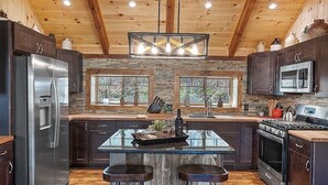 Une cuisine moderne avec des meubles en bois foncé, des appareils en acier inoxydable, un îlot central doté de tabourets et de grandes fenêtres.