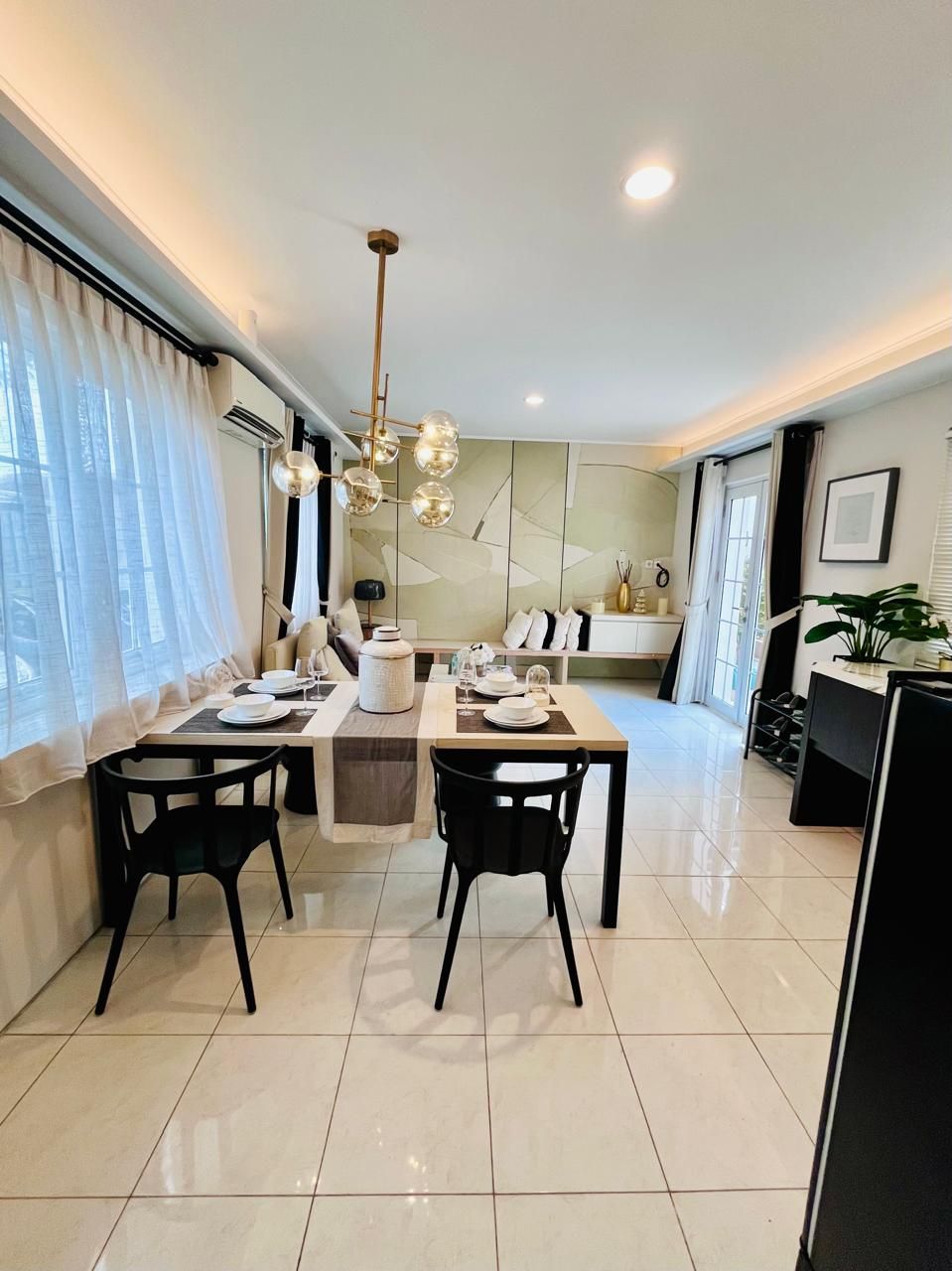 A modern dining area with a table set for two, a chandelier, and a view of the living room.