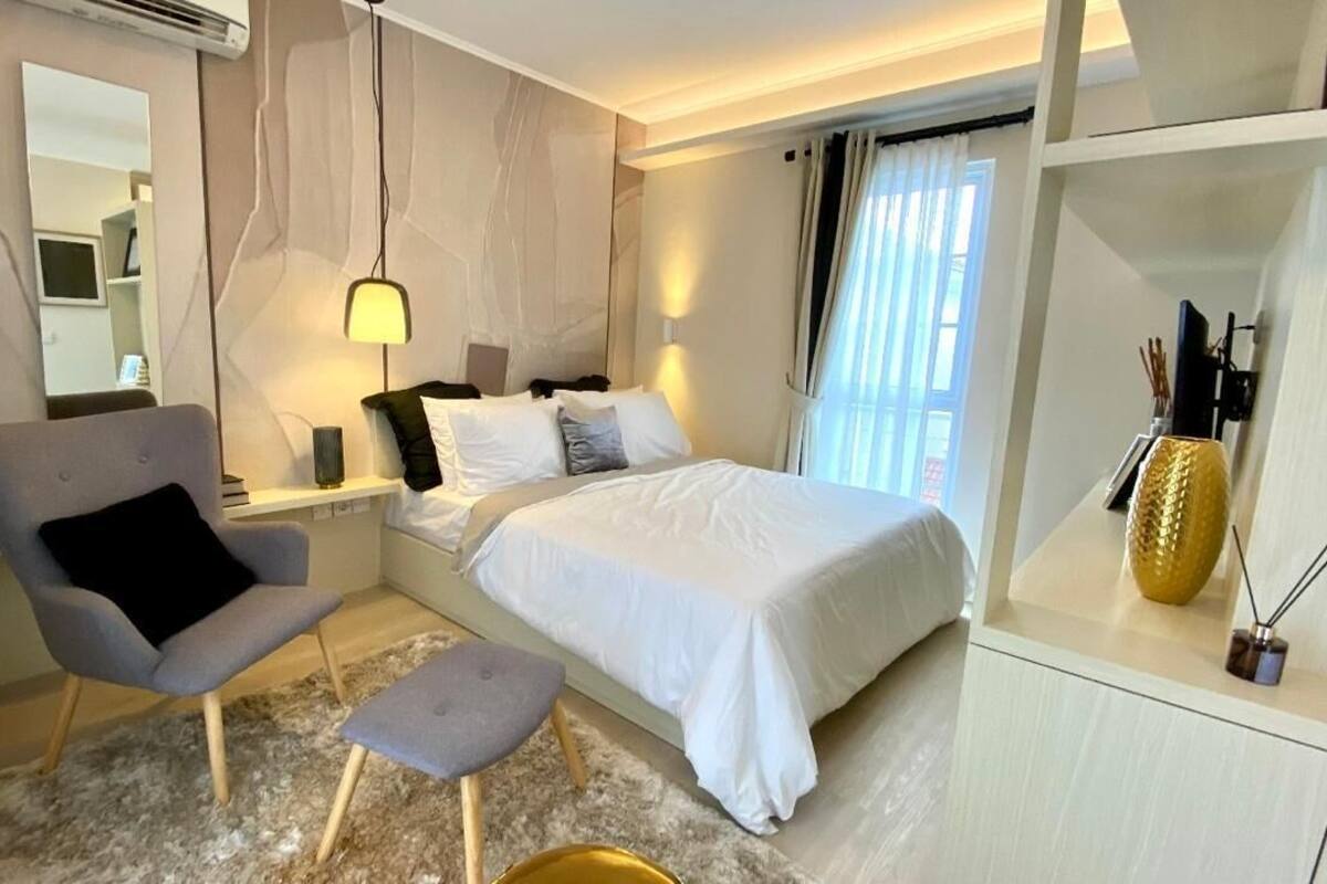 Ein modernes Hotelzimmer mit einem Bett, einem Sessel, einem kleinen Tisch und einer Ablage mit Dekoration.