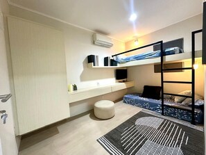 Een compacte kamer met stapelbedden, een bureau met een computer en een klein, rond voetenbankje.