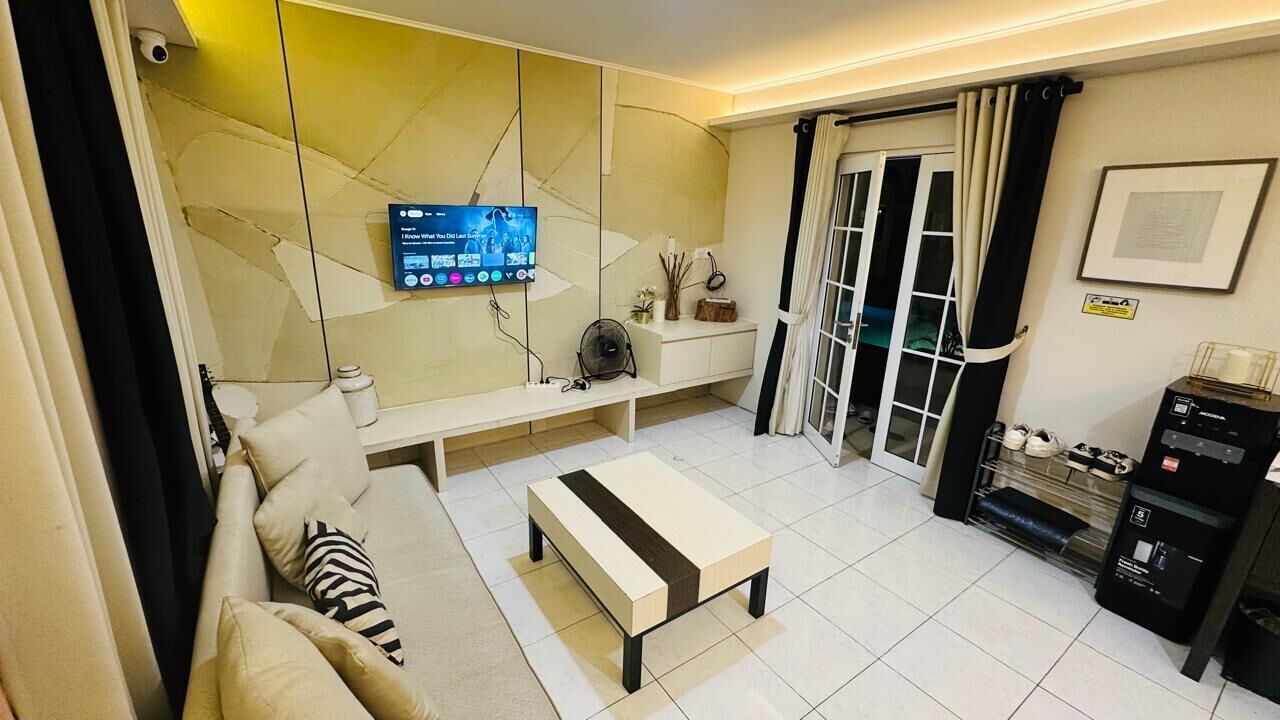 Uma sala de estar moderna com um sofá, uma mesa de centro, uma televisão de tela plana na parede, um ventilador e um sapateiro.
