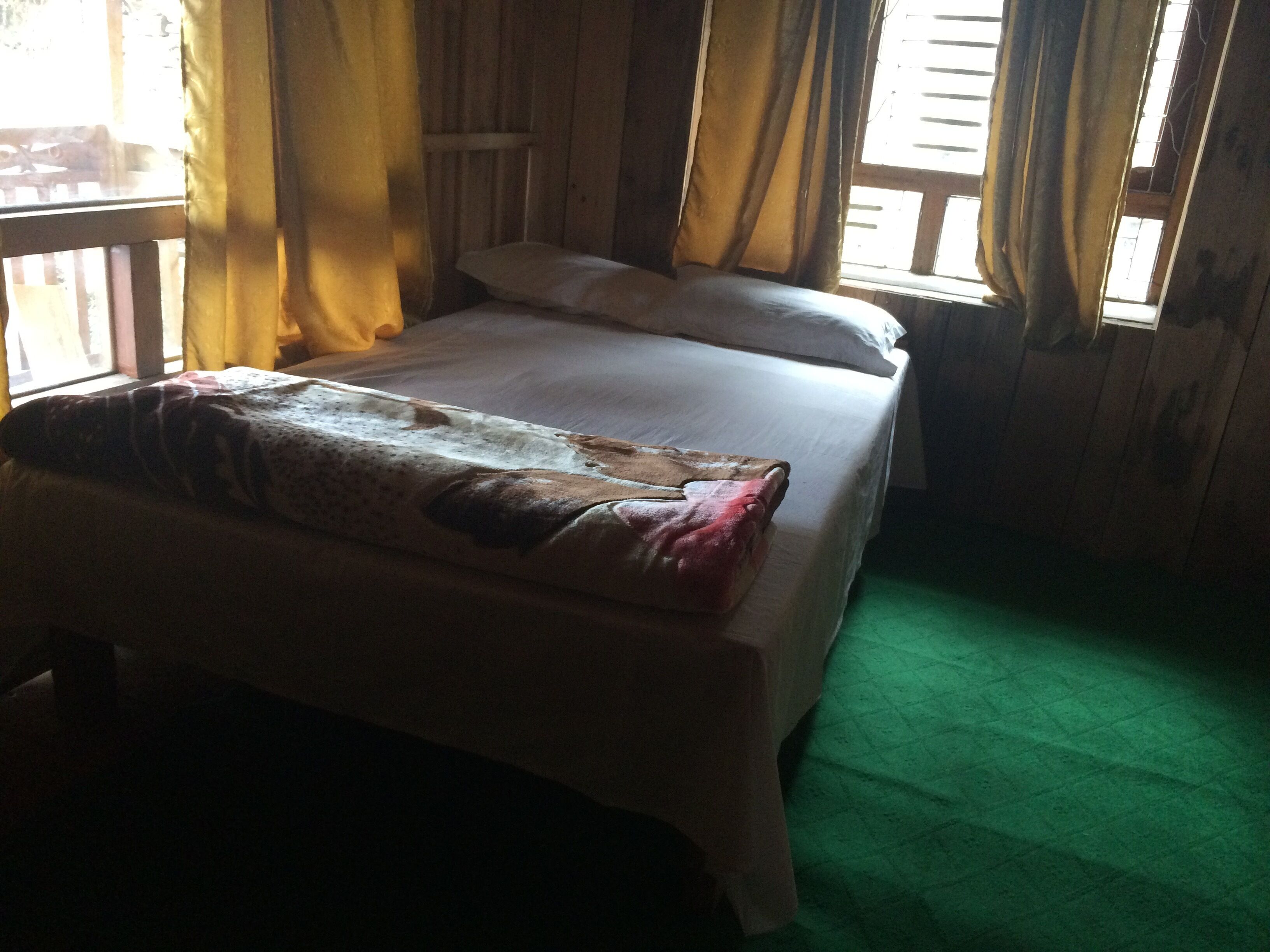 Una habitación con una cama, un ventanal con cortinas y una alfombra verde.