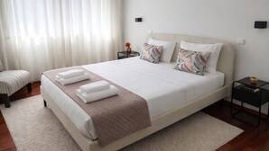 A neatly made bed with towels, a bedside table with a vase, and a chair.