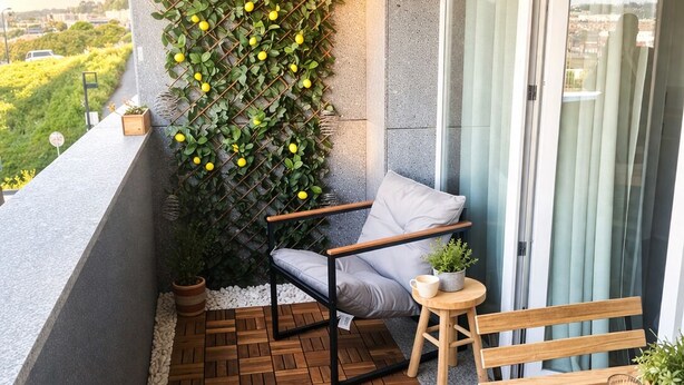 A balcony with a wooden floor, a cushioned chair, a small table with a plant, and a wall-mounted plant arrangement.