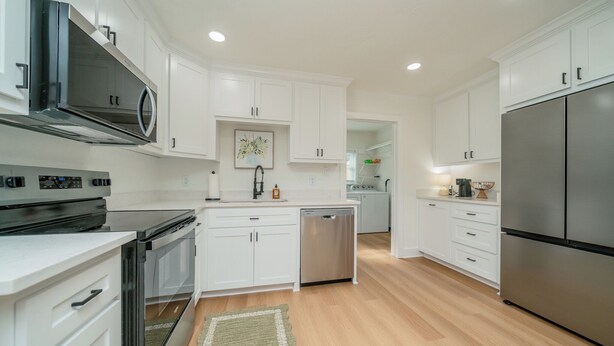 A modern kitchen with white cabinets, stainless steel appliances, and a wooden floor. - Charming 2-bedroom house in Kilgore (Kilgore)
